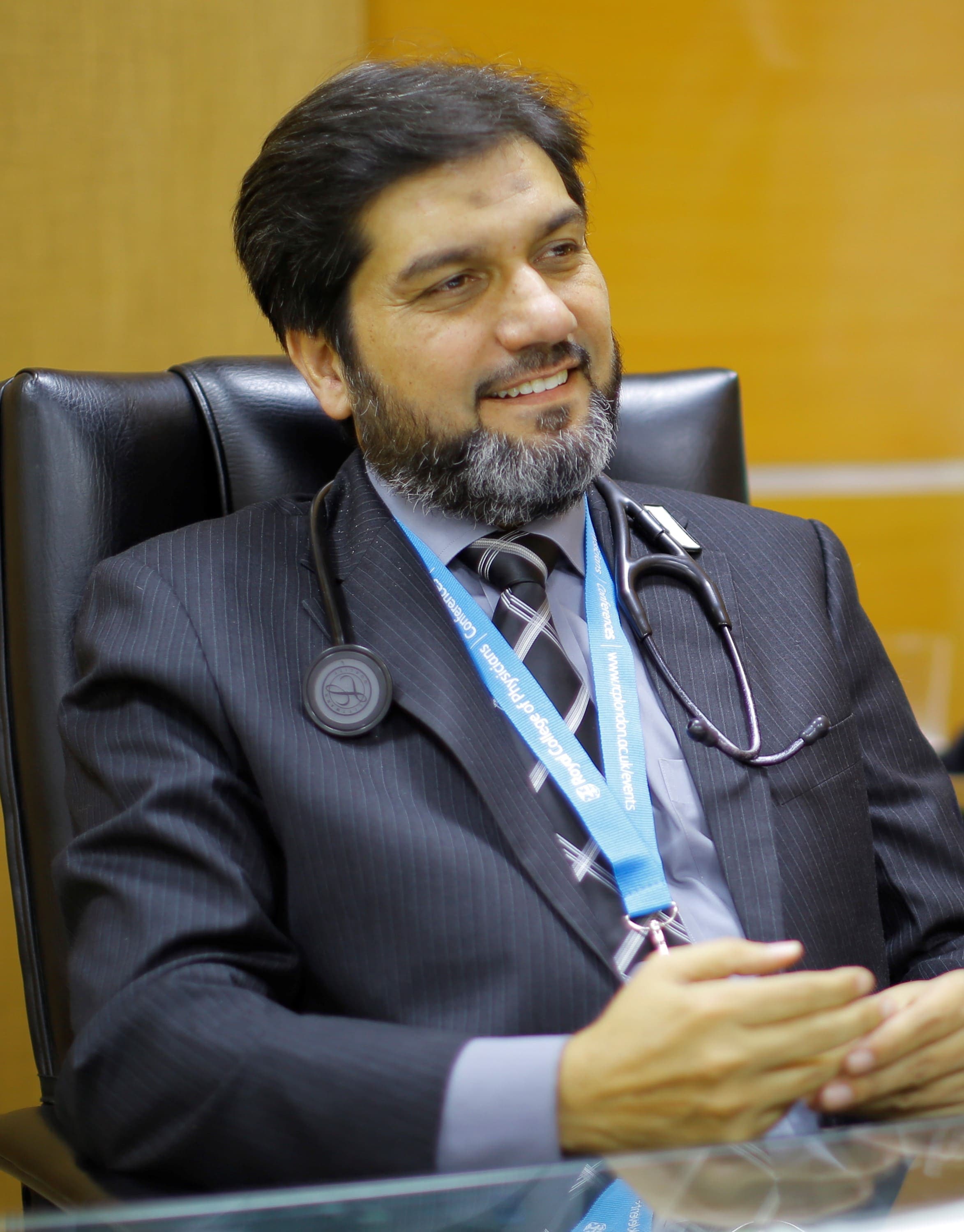 Dr. Asim Rana seated in a suit wearing a conference lanyard and stethoscope